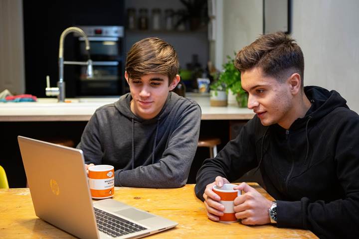 Two Teen Boys Looking At Laptop At Table Looking Jovial